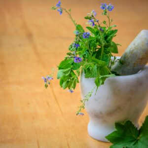 Marble mortar and pestle with fresh herbs and flowers on wooden table enhancing natural health and cooking aesthetics.
