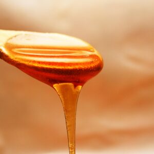 Close-up of honey dripping from a wooden spoon, showcasing its rich texture and color.